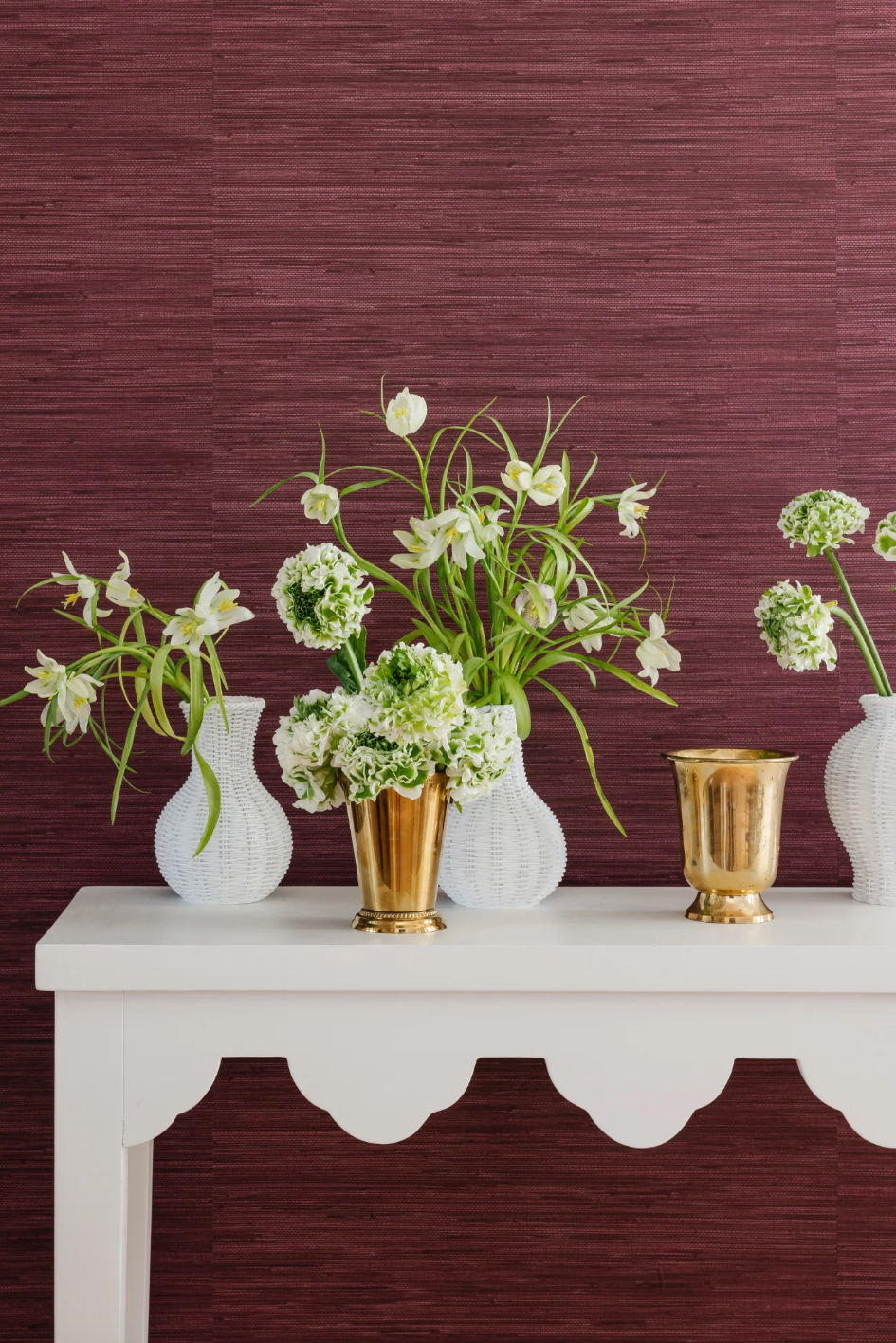 arrangement av blomster i dekorative vaser på et hvitt bord mot en strukturert lilla vegg