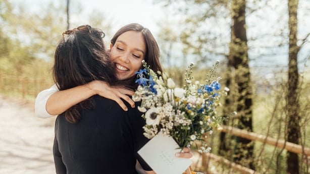 Brud holder blomsterbukett, kurv og konvolutt mens han klemmer venn