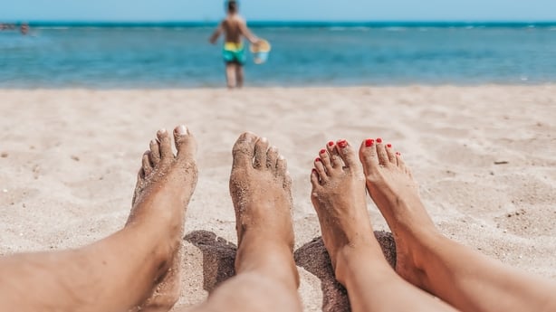 Sandete tær og føtter av et par som nyter en strandferie mens du ser på ungen sin leke i sanden.