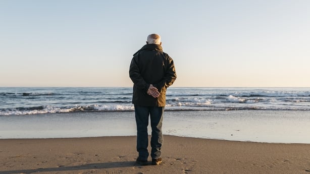 Pensjonert eldre mann som rusler på stranden om vinteren. 