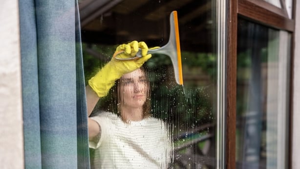 Et kvinne som rengjør vinduet glass med landsted med en squegee. Fotografert gjennom vindu