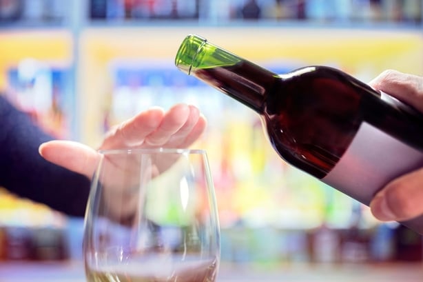 En kvinne legger en hÃ¥nd over vinglasset sitt mens noen gÃ¥r for Ã¥ skjenke mer vin til henne