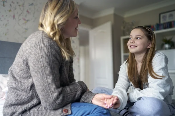 Moden mor sitter på sengen med en tenåringsdatter hjemme iført kjeveortodontiske tannregulering og snakker og ler
