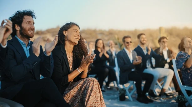 Spente gjester som sitter på et utested og klapper i hendene. Multietnisk vakker mangfoldig folkemengde som feirer en begivenhet, et bryllup eller en konsert. Inspirerende dag med vakkert varmt vær.