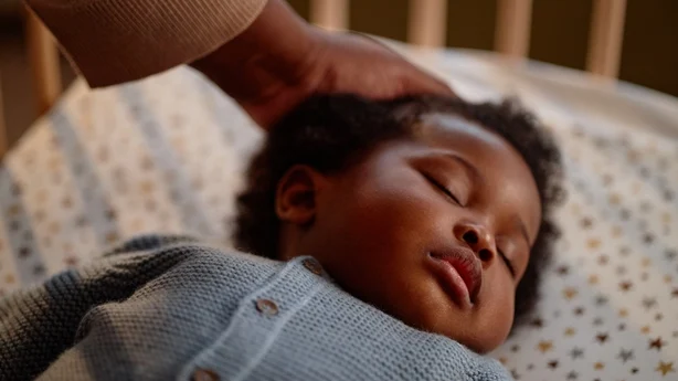 Nærbilde på det fredelige ansiktet til den svarte jentebabyen som sover i barneseng mens mødre forsiktig kjærtegner barnas hår på barnas soverom