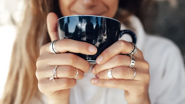Nærbildehånd av kvinne som holder en kaffekopp og har på seg sølvringer