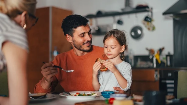 Et søtt smilende kaukasisk barn som spiser et måltid sammen med familien.