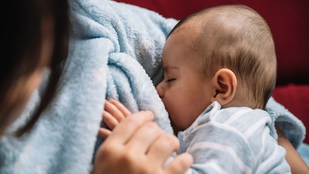 Mor som ammer babyen sin på sofaen