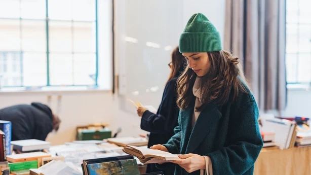 Vakker kvinne handler brukte bøker i bruktbutikk, bruktbokhandel. Generasjon Z-studenthandel på loppemarked. Konsept for resirkulering, upcycling og miljømessig bærekraft.