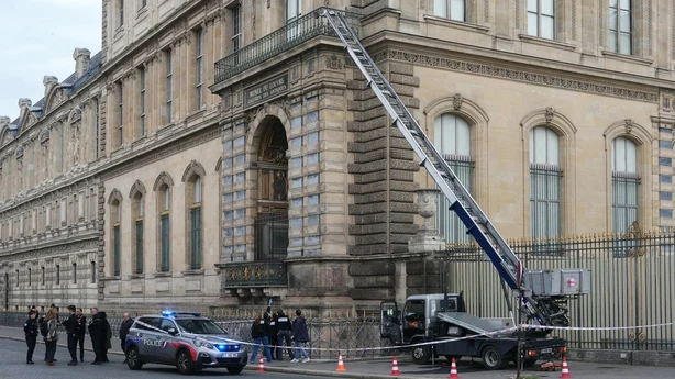 En stige festet til en lastebil stÃ¥r ved siden av en stor beige og grÃ¥ bygning. En politibil og flere politifolk stÃ¥r ved siden av.