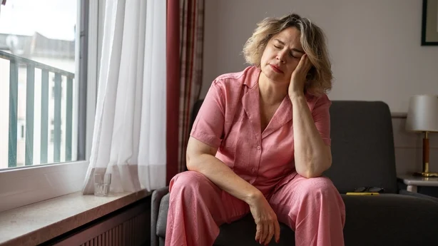 Moden kvinne som lider av hodepine og holder hodet med hendene mens hun sitter på sofaen hjemme. Menopause og depresjon. Psykisk helse konsept