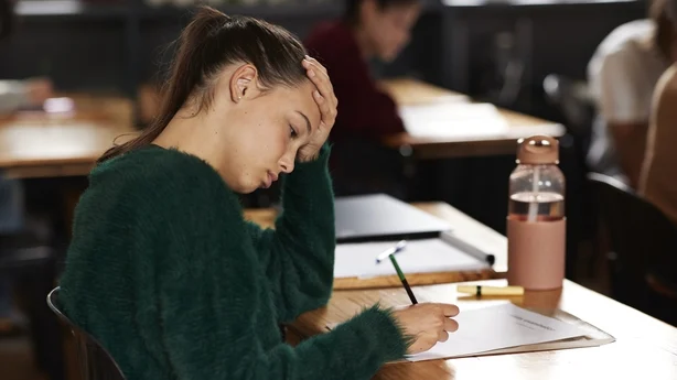 Spent tenåringsjente skriver på papir mens hun sitter ved pulten under eksamen i klasserommet