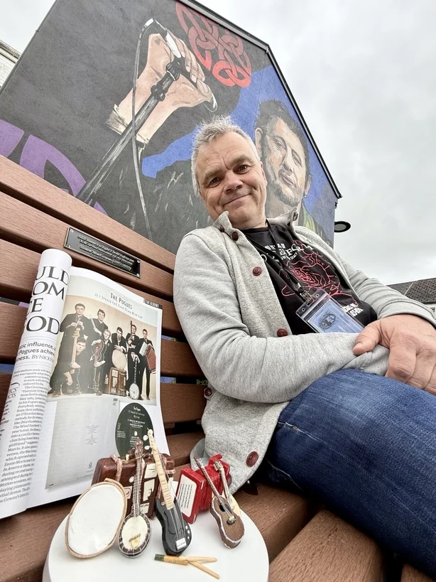 Turist Gerret Lorenzen sitter ved siden av et utvalg modellinstrumenter som sitter under et fotografi av The Pogues