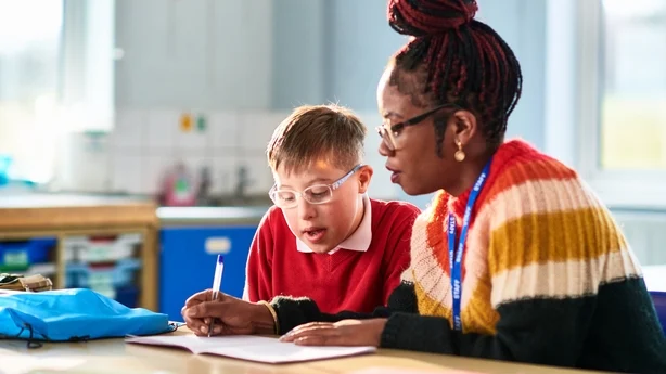 Kvinnelig støttearbeider som bistår barn med spesielle pedagogiske behov, skriver i boken sin mens han ser på og konsentrerer seg