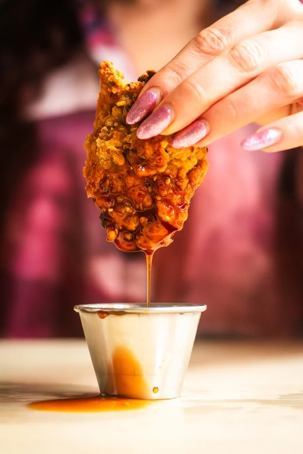 Nærbilde av stekt kylling som dyppes i saus