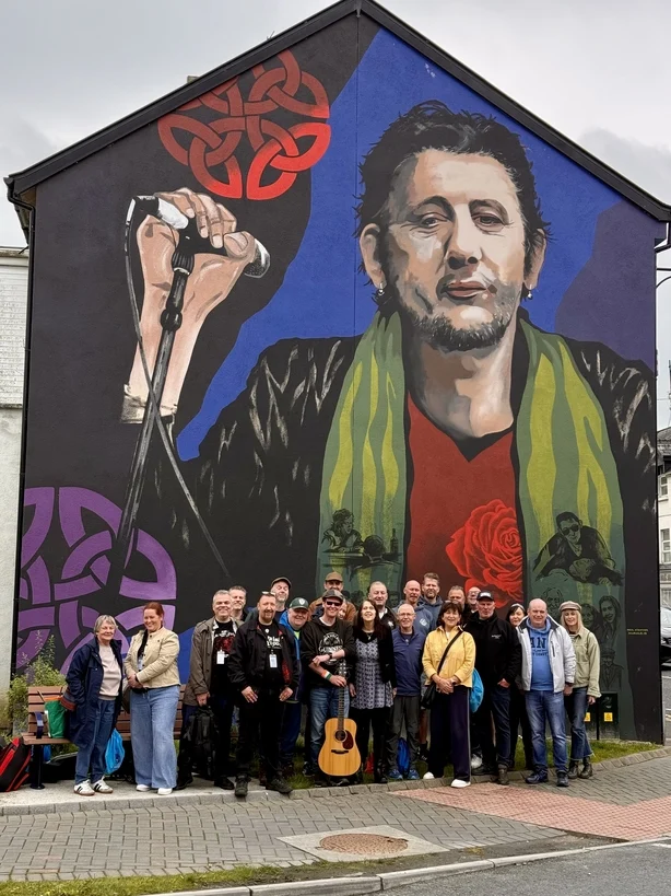 En gruppe turister stÃ¥r foran et Shane MacGowan-veggmaleri