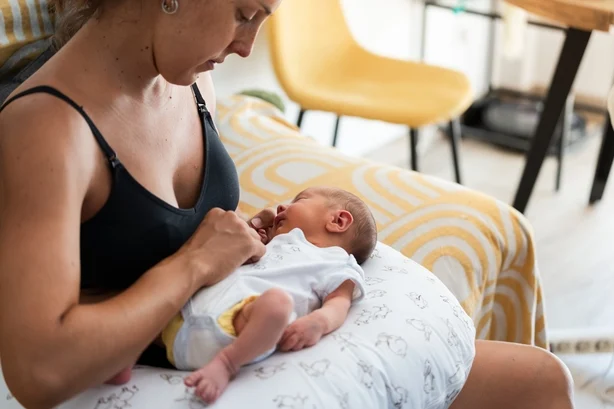 Ung mor sitter komfortabelt mens hun holder sin nyfødte baby på en ammepute