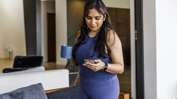 kvinne iført athleisure wear drikker kaffe og ser på telefonen