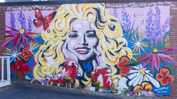   Blomster er lagt ved siden av et veggmaleri av countrysangerinnen Dolly Parton 