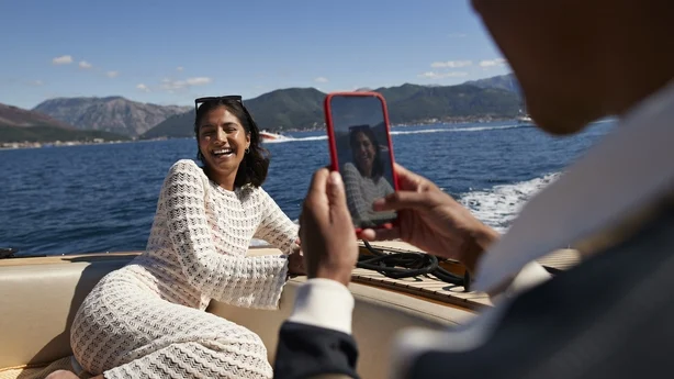 Mann som fotograferer glad kjæreste på mobiltelefon i motorbåt i sommerferien