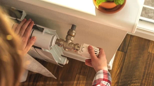 Kvinne justerer temperaturen på ventilen til en radiator hjemme